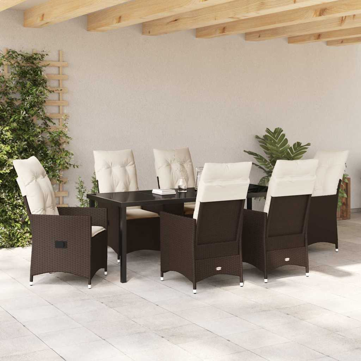 Essgruppe im Freien mit dunkelbraunen Korbstühlen und cremefarbenen Kissen um einen schwarzen Tisch auf einer Terrasse. Grün im Hintergrund.