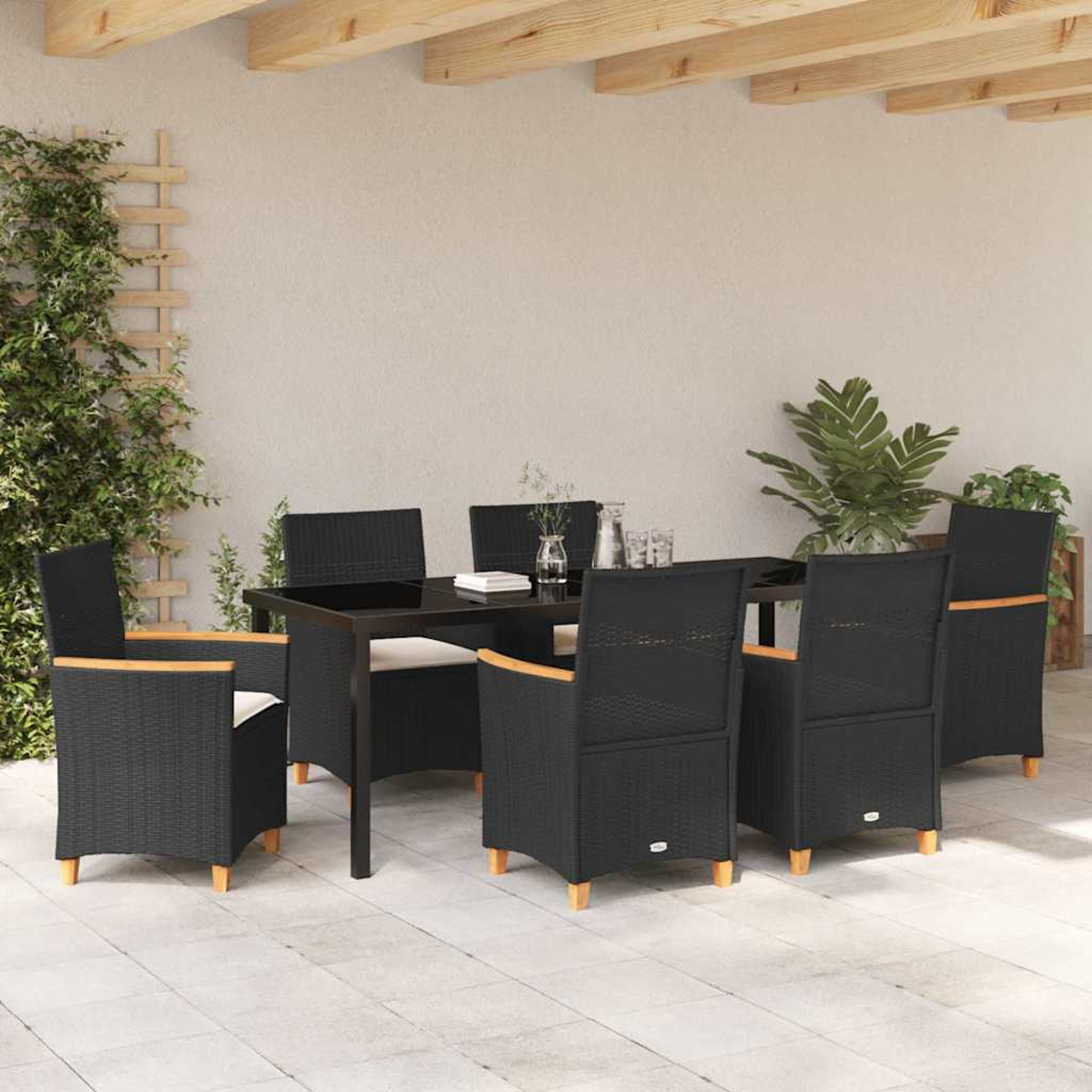 Essgruppe im Freien: schwarze Stühle um einen Tisch, Pflanzen, Holzbalken. Eine sonnige Terrassenszene.