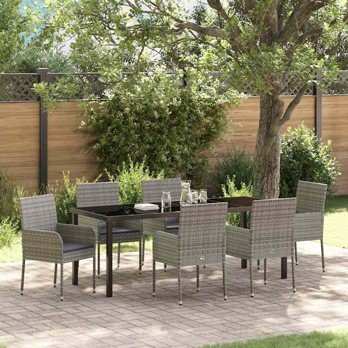 Eine Terrasse mit Tisch und sechs Stühlen. Ein Holzzaun und Bäume sind im Hintergrund. Gläser und eine Kanne stehen auf dem Tisch.