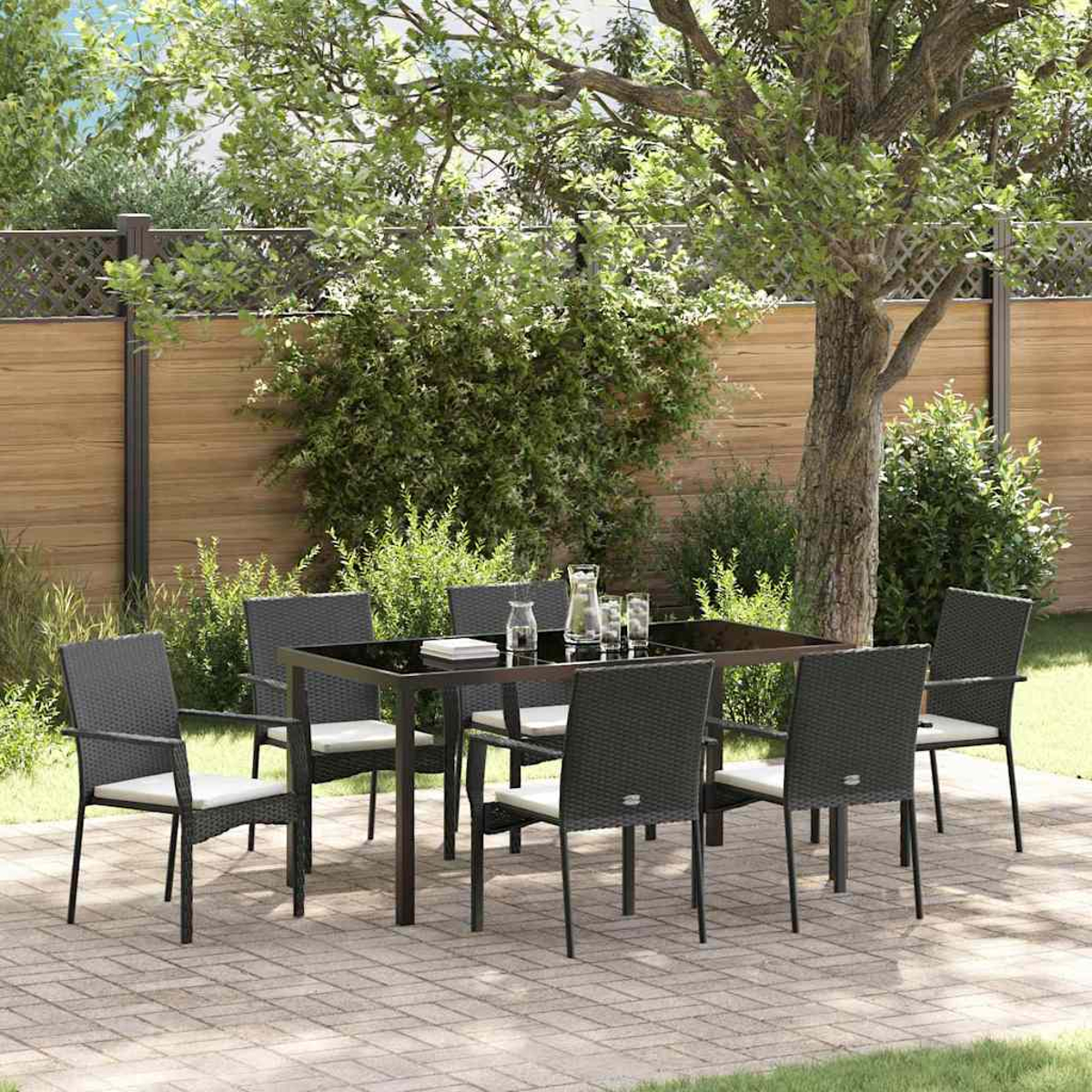 Essgruppe im Freien mit Tisch und Stühlen. Ein Baum und Büsche sind im Hintergrund. Der Boden ist gepflastert.