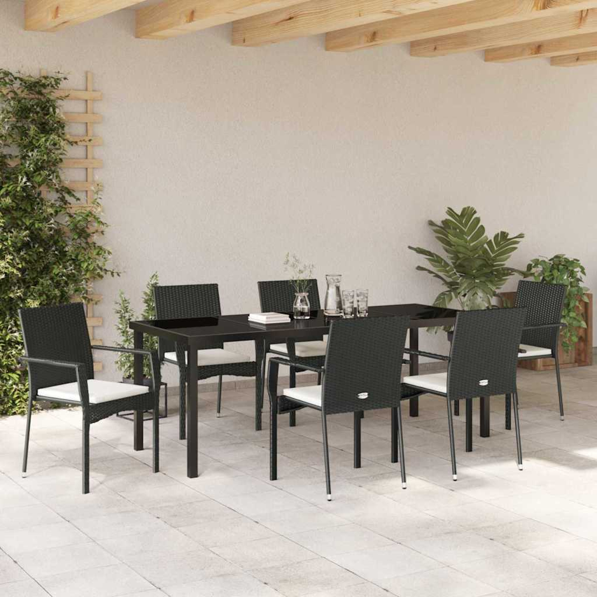 Ein Terrassenset mit einem schwarzen Tisch und Stühlen. Links Pflanzen und ein Spalier. Helle Wand und Holzbalken oben.