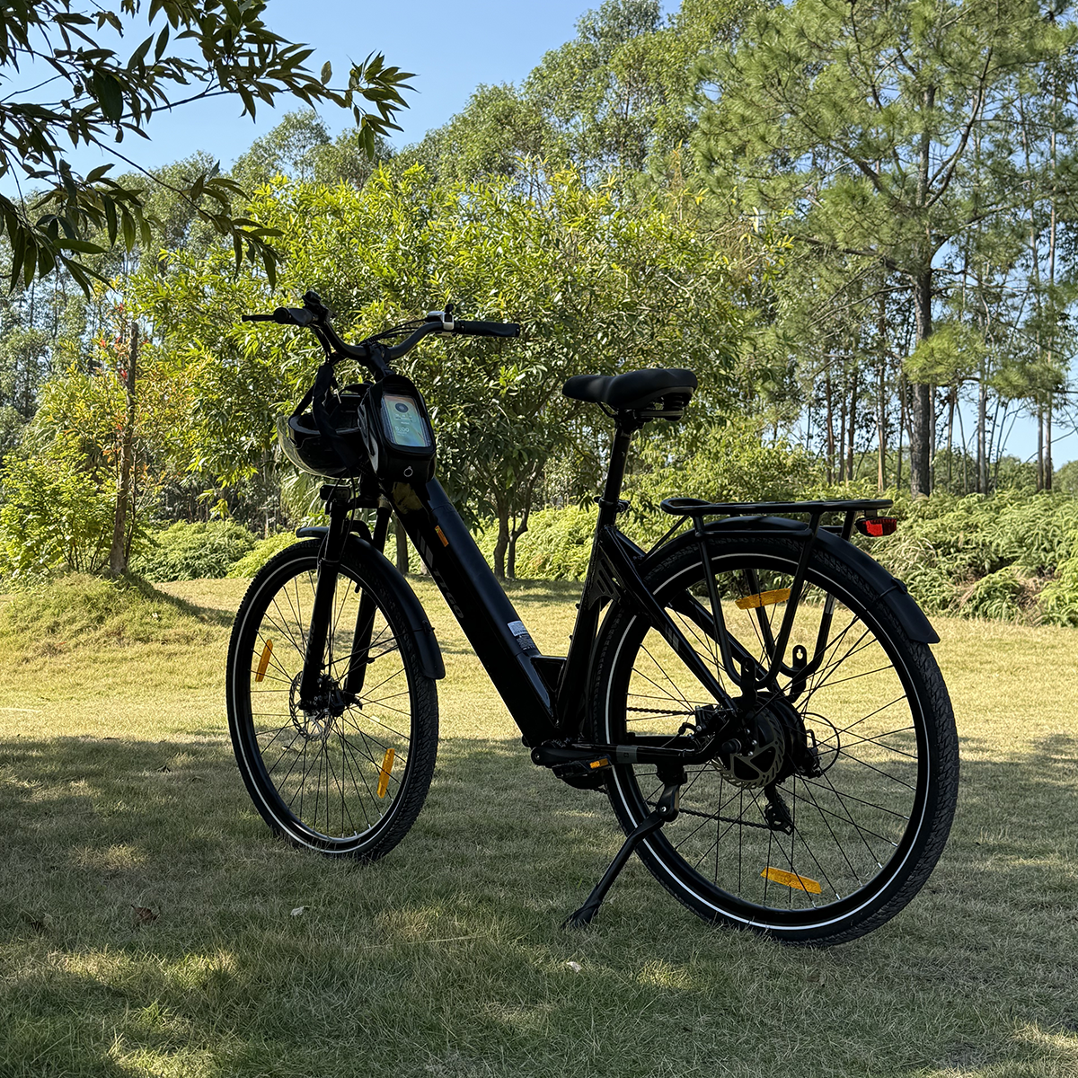 Czarny rower elektryczny zaparkowany na trawie. W tle drzewa i niebo.
