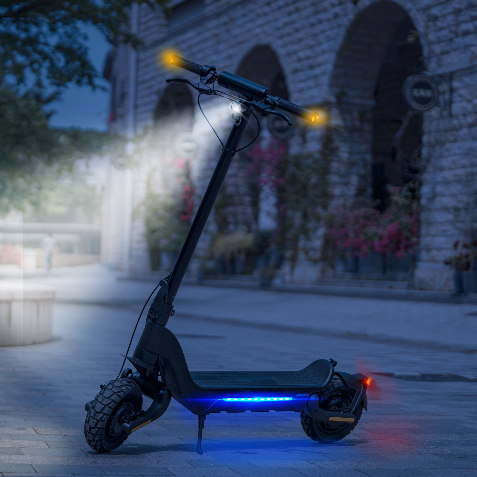 Czarna hulajnoga elektryczna ze światłami na brukowanej ulicy nocą. Budynki w tle.