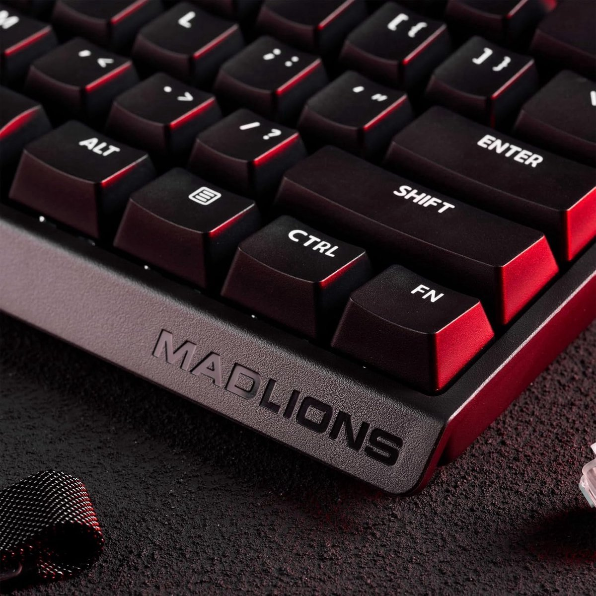 Primo piano di una tastiera Mad Lions nera con dettagli rossi. Tasti includono Ctrl, Shift, Enter e Alt. Superficie nera e poggiapolsi nero.