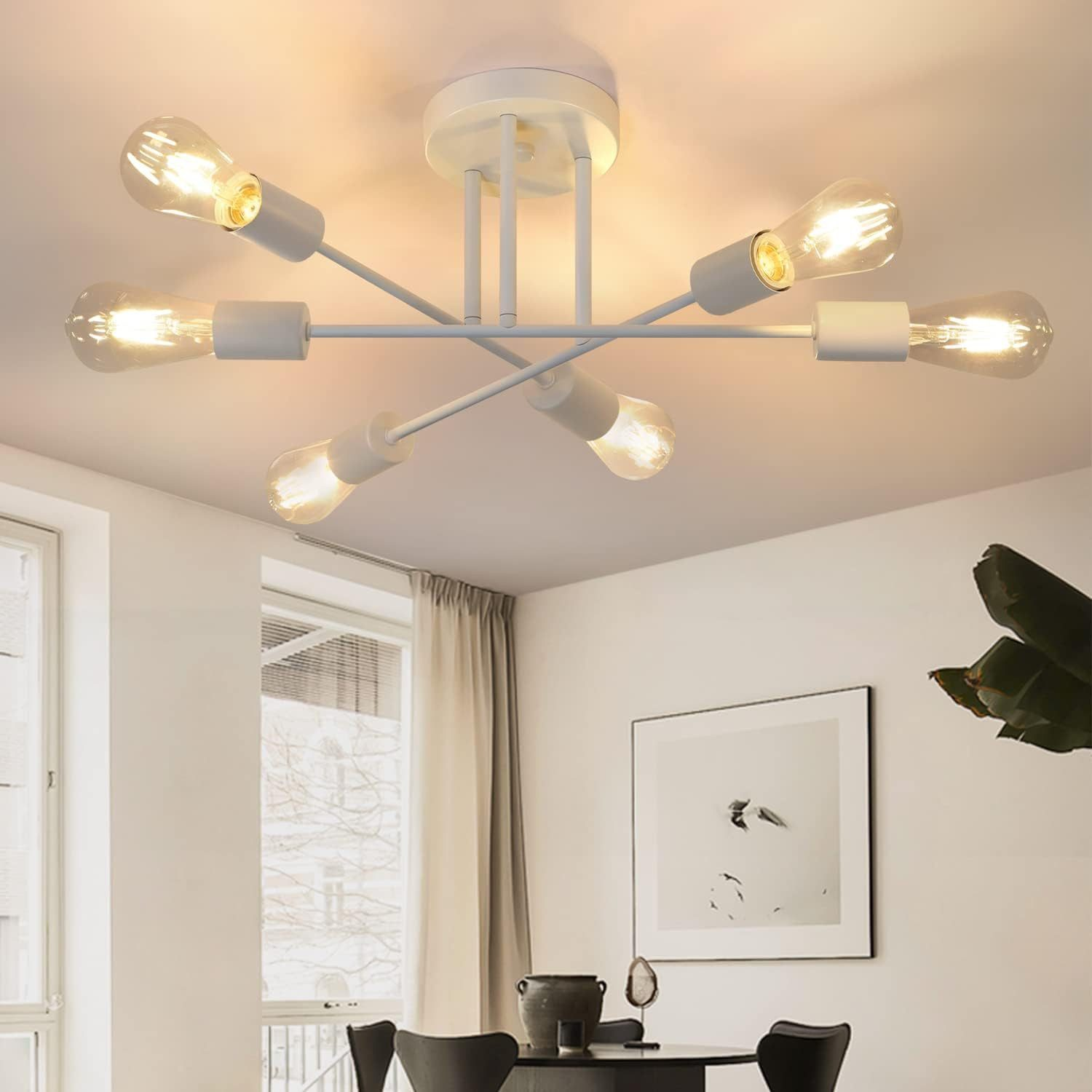 Biała lampa sufitowa z sześcioma żarówkami jest zamontowana na suficie. Poniżej stół z krzesłami. Oprawiony obraz wisi na ścianie.