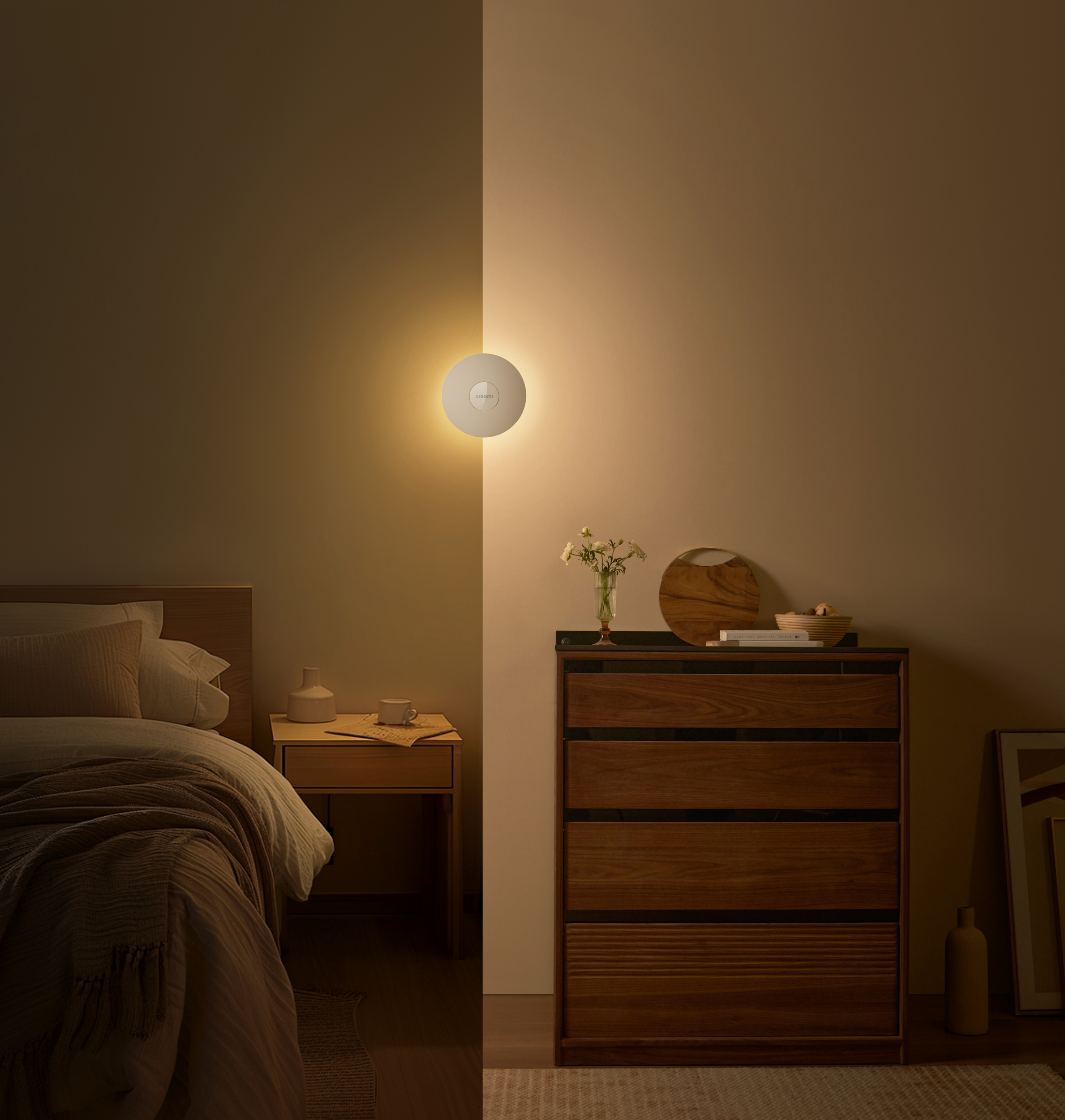 Ein Schlafzimmer mit Wandleuchte, Bett und Holzkommode. Eine Tasse auf einem Tisch ist ebenfalls sichtbar.