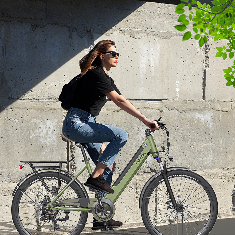 Mujer con gafas de sol monta en bicicleta verde. Lleva camisa negra y vaqueros. Pared de hormigón al fondo, con hojas en la esquina.