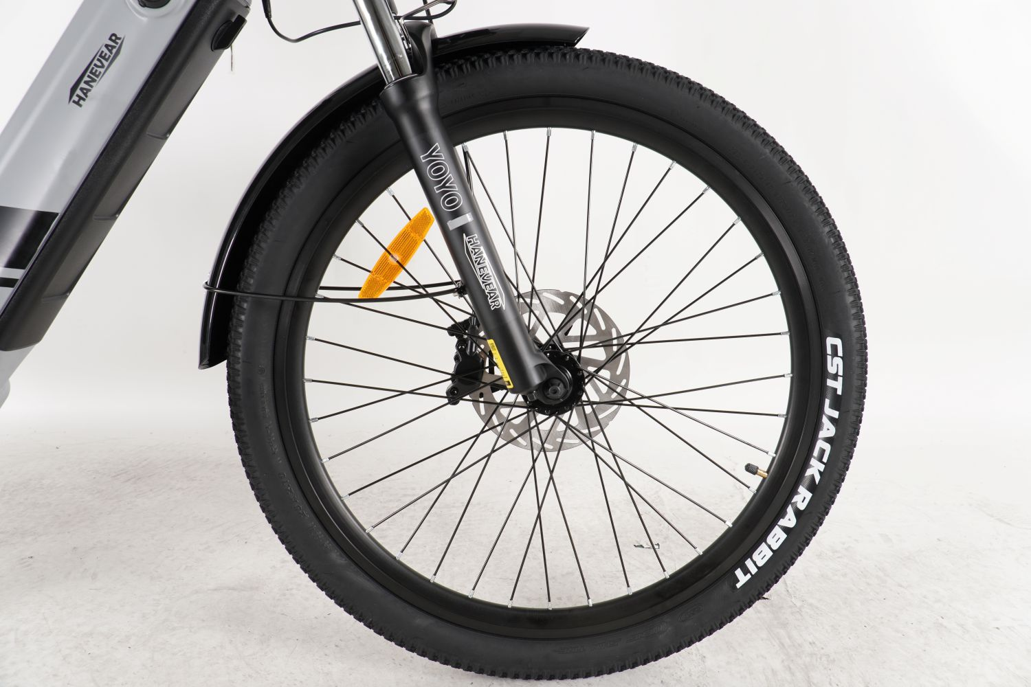 Rueda delantera de una bicicleta negra. El neumático dice 'CST Jack Rabbit'. Se ve una horquilla plateada con 'HANEVEAR'.