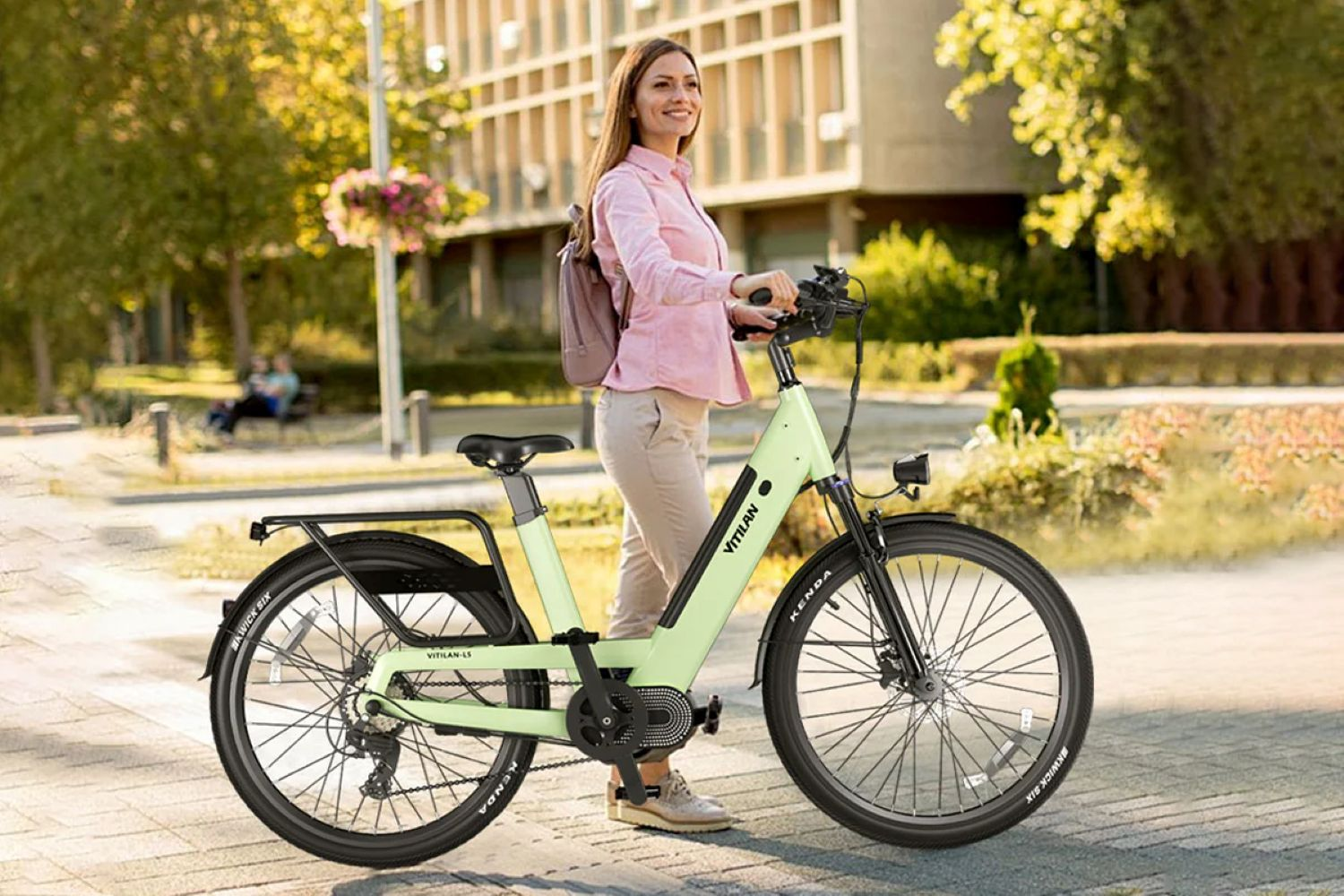 Una mujer sonríe, de pie junto a una bicicleta eléctrica verde claro, frente a un edificio y árboles.