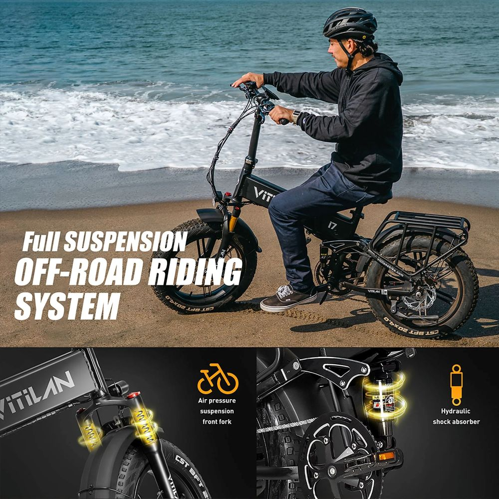 Hombre montando una bicicleta eléctrica negra en una playa. La bicicleta tiene llantas anchas. El fondo muestra el océano y la arena.