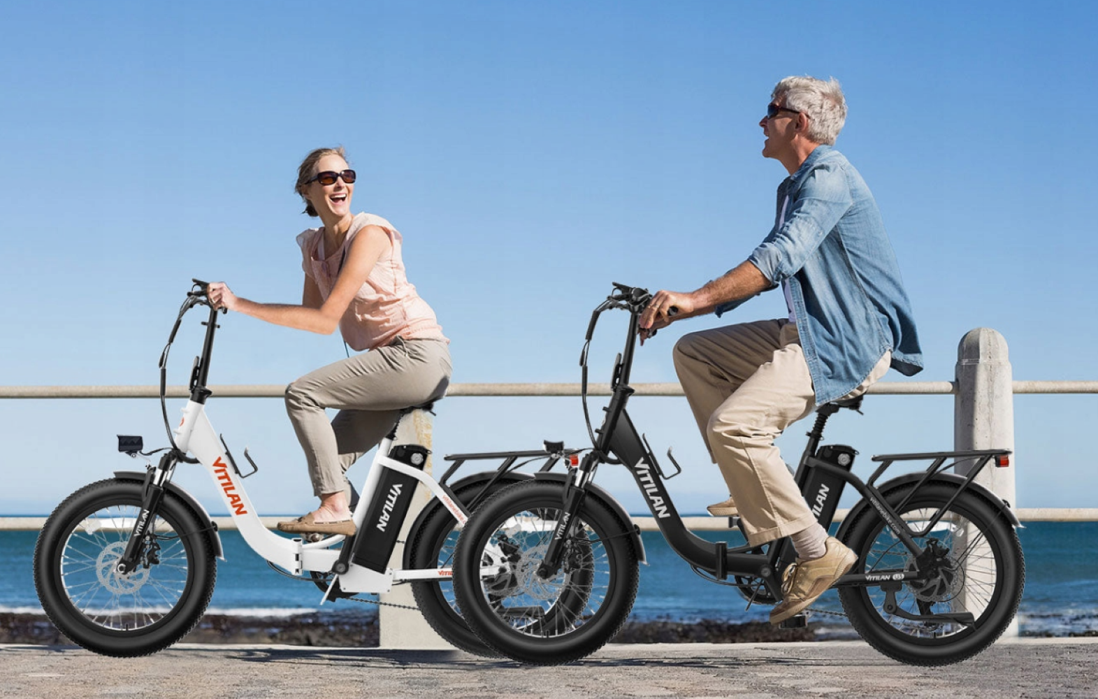 Una pareja monta en bicicletas VILIAN en un día soleado. Sonríen, con gafas de sol, montando por un camino costero.