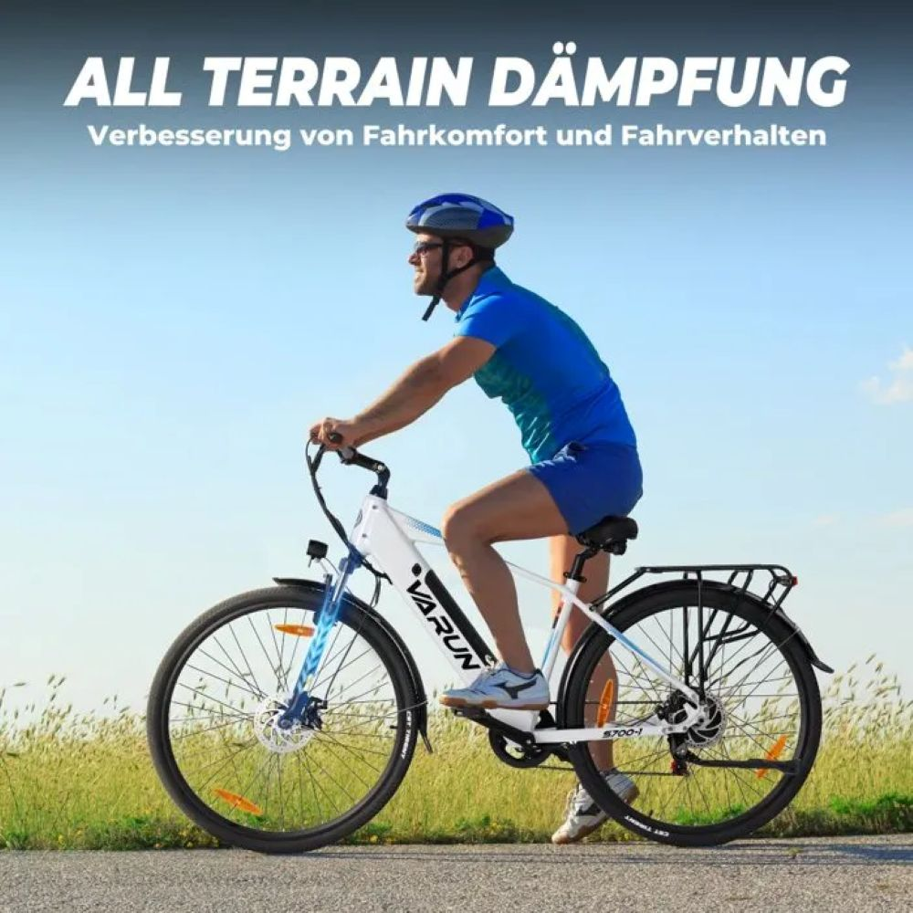 Un hombre anda en bicicleta eléctrica blanca y negra en un día soleado. Lleva casco y ropa deportiva azul. La bicicleta tiene escrito VARUN.
