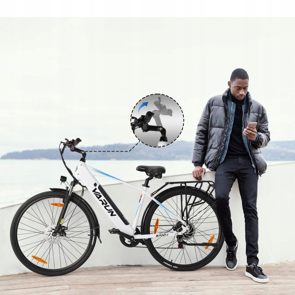 Un hombre está junto a una bicicleta eléctrica blanca. Sostiene un teléfono y lleva una chaqueta. La bicicleta tiene un neumático negro y detalles azules.