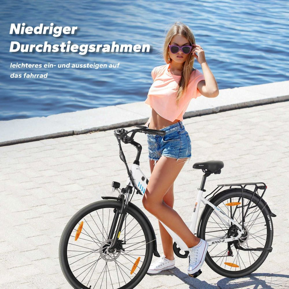 Una mujer junto a una bicicleta blanca. Usa top rosa, shorts de mezclilla y gafas de sol. El fondo es el mar.
