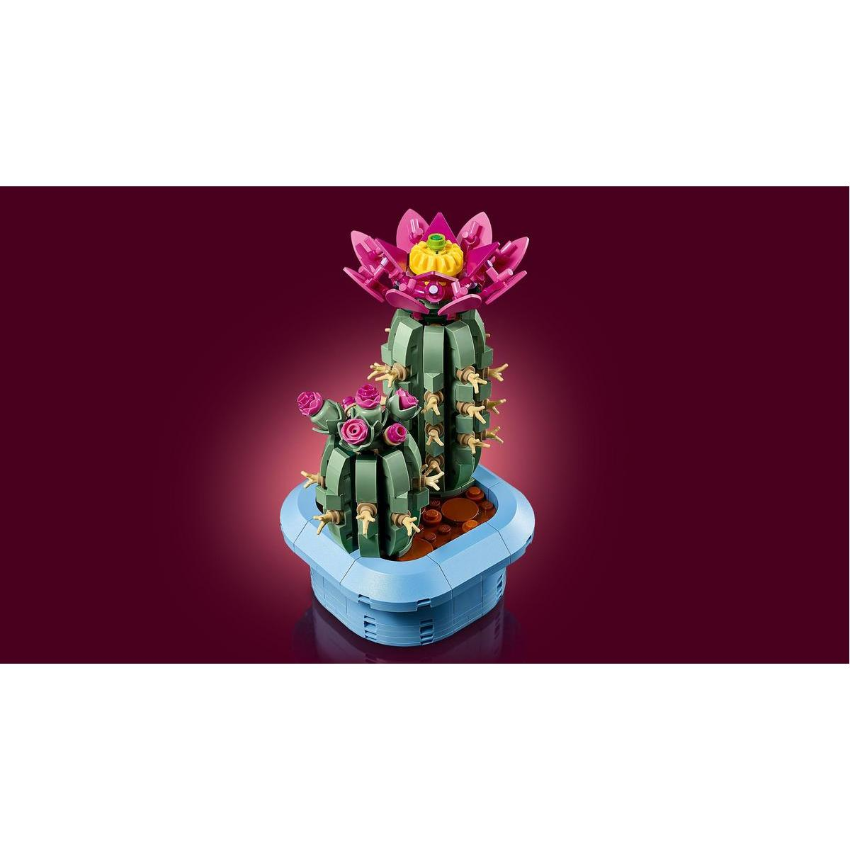 Zestaw kaktusów Lego w niebieskiej doniczce, z różowymi kwiatami i dużym różowym kwiatem. Zielone części kaktusa i bordowe tło.