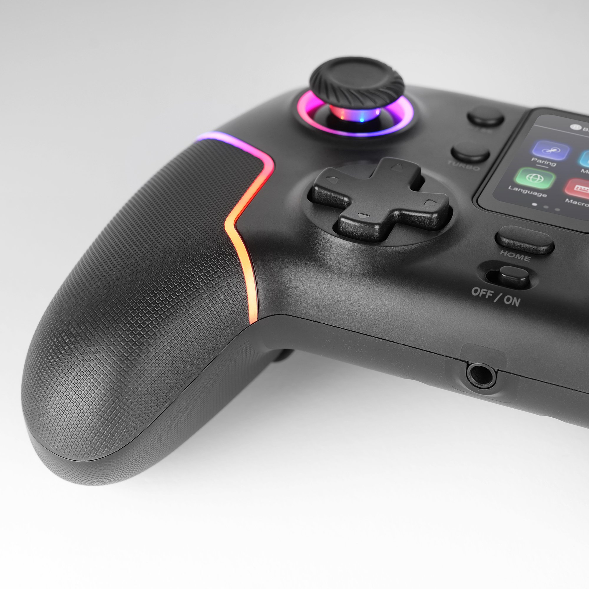 Mando de juegos negro con bordes y botones brillantes. Incluye joystick, cruceta y pantalla con iconos. Fondo blanco.