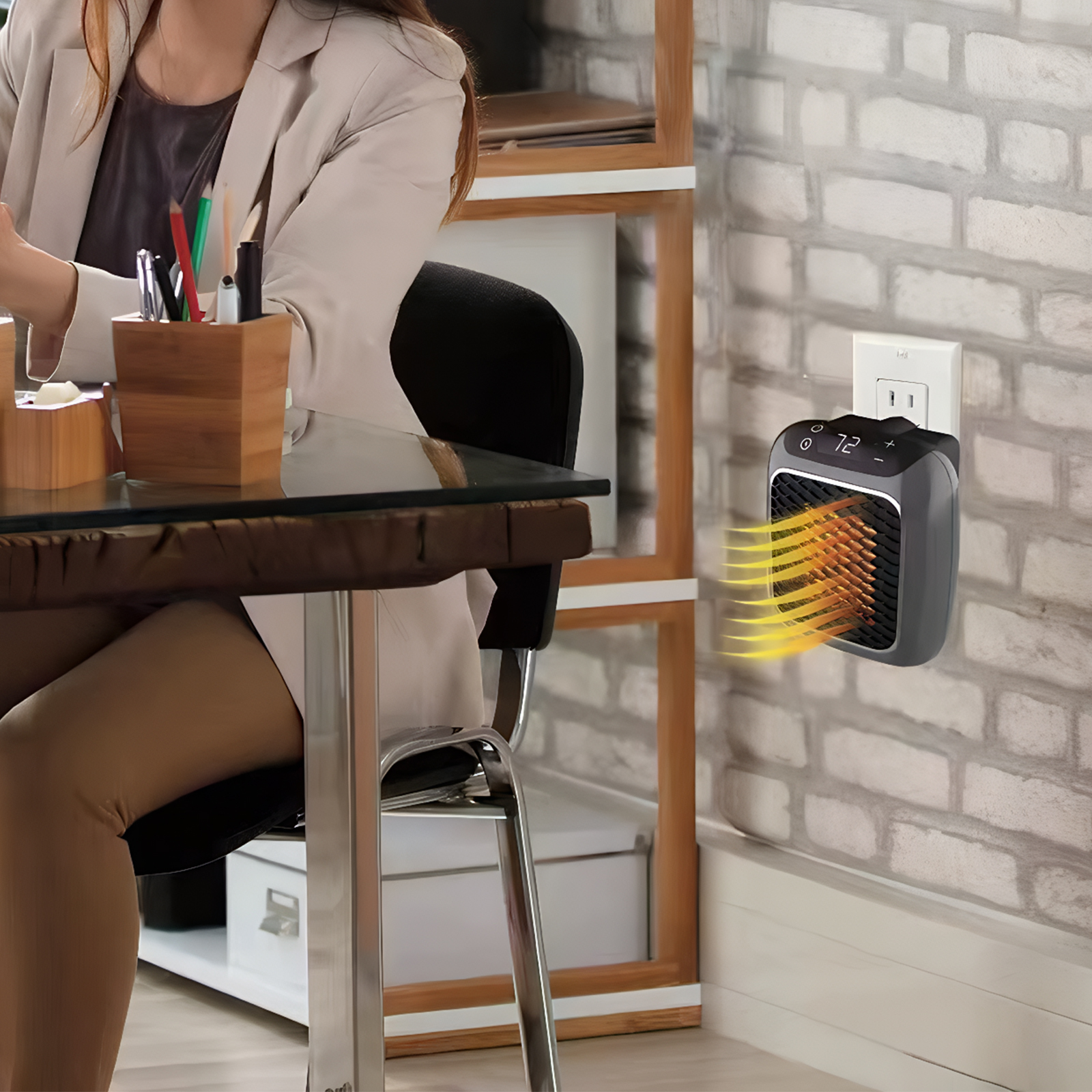 Eine Frau sitzt an einem Schreibtisch. Ein kleiner Heizlüfter ist an der Wand eingesteckt. Der Heizlüfter ist eingeschaltet.