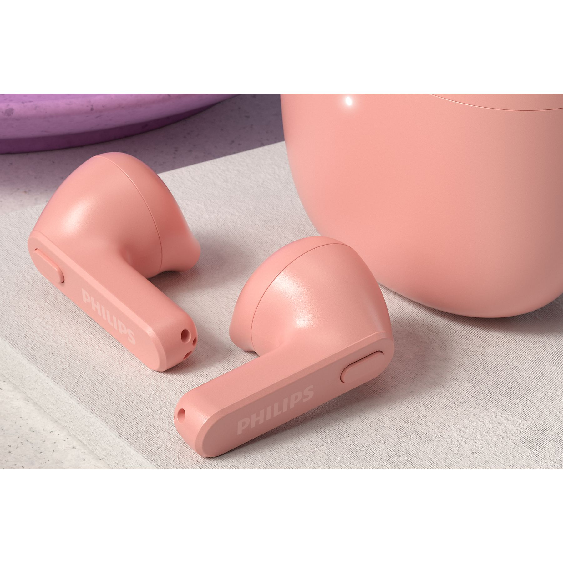 Auriculares Philips rosas sobre una superficie texturizada. Un componente rosa más grande en el fondo. Los auriculares están en ángulo.