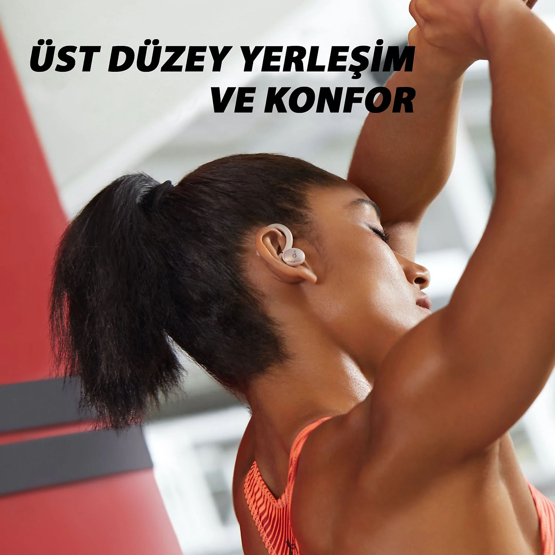 Mujer en ropa de entrenamiento con auriculares, brazos arriba. Texto: 'Ubicación y confort de alto nivel'.