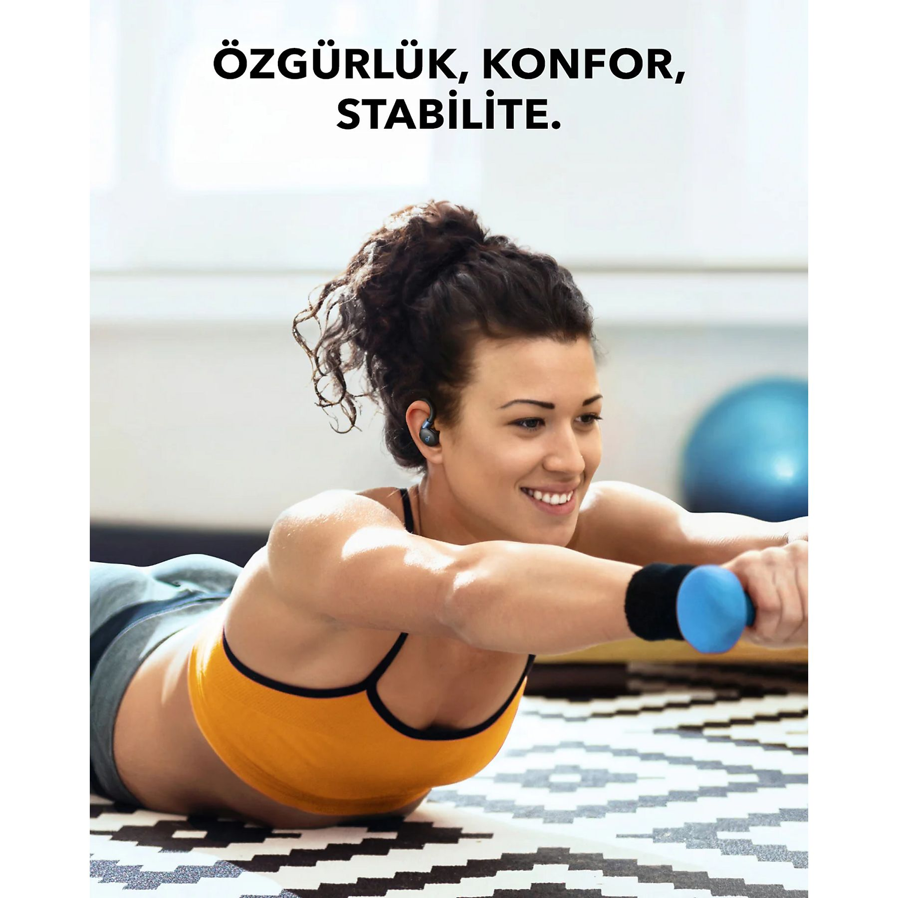 Kobieta ćwiczy z hantlami, w słuchawkach. Tekst: wolność, komfort, stabilność. Czarno-biała wzorzysta podłoga.