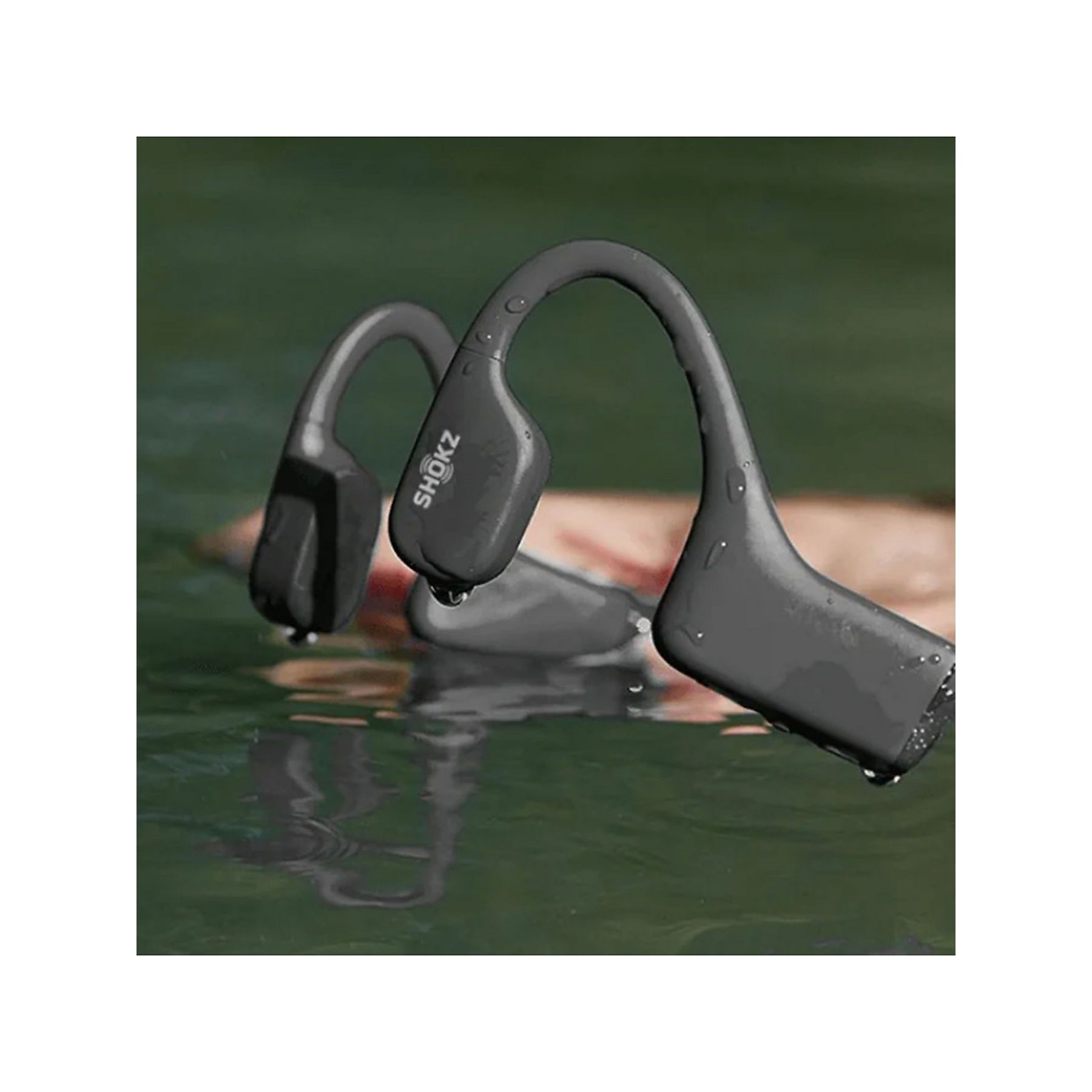 Szare słuchawki Shokz częściowo zanurzone w wodzie, z widocznym brandingiem. Krople wody przylegają.