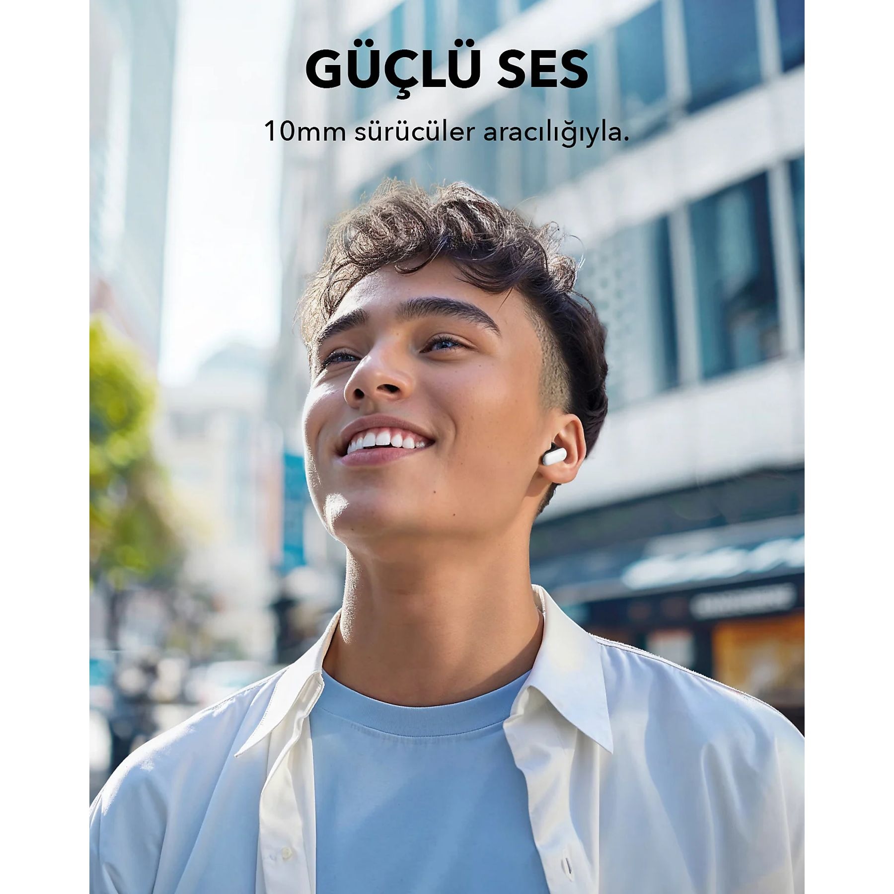 Un uomo sorridente con auricolari si trova in una città. Indossa una camicia bianca sopra una camicia blu.