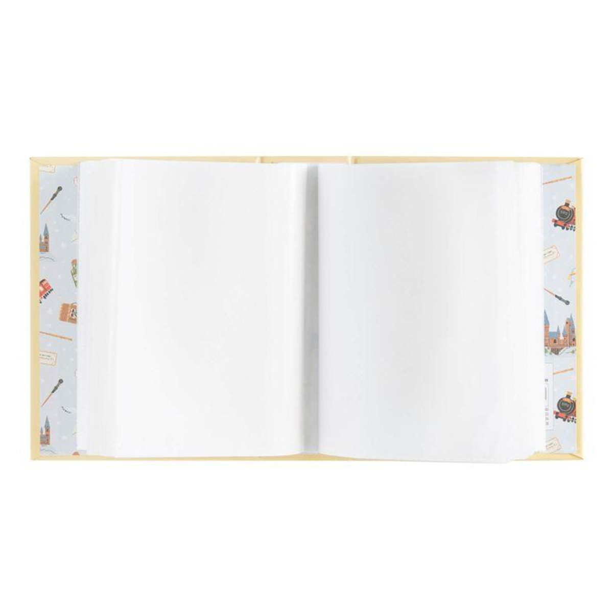 Livre ouvert avec pages blanches. La couverture a un motif bleu clair avec des illustrations de châteaux, baguettes et trains.