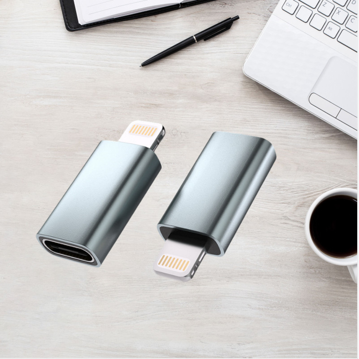 Zwei silberne Adapter auf einem Holztisch. Einer hat einen USB-C-Anschluss, der andere einen Lightning-Anschluss. Stift, Notizbuch, Laptop und Kaffee in der Nähe.