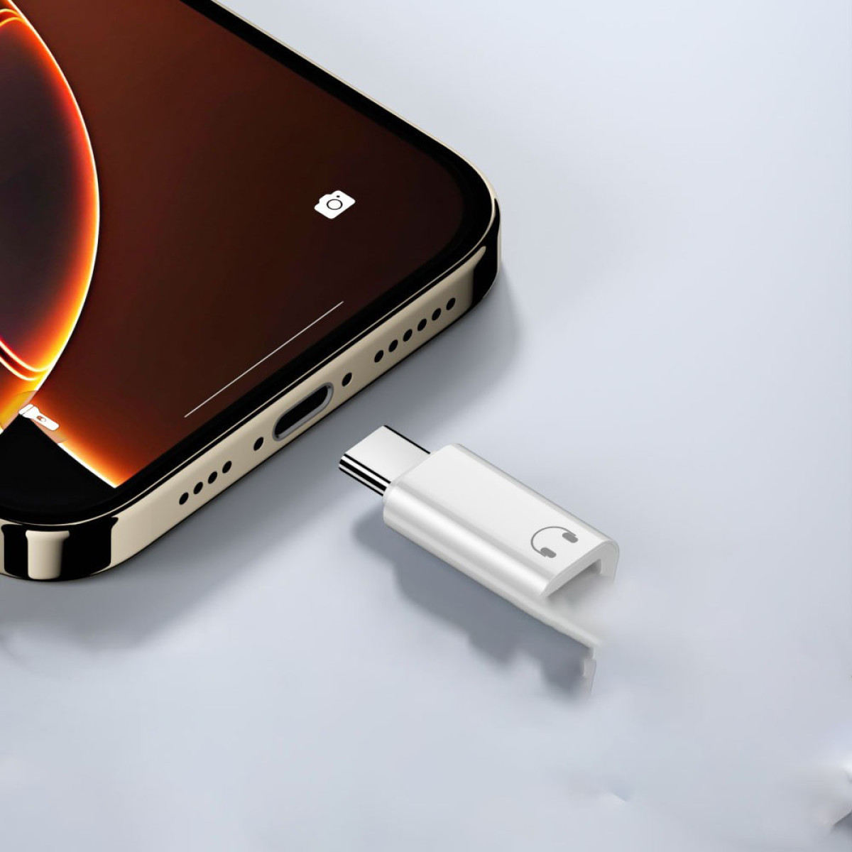 Ein Smartphone und ein weißer Adapter liegen auf einer hellen Oberfläche. Der Adapter hat einen USB-C-Anschluss und ein Kopfhörersymbol.