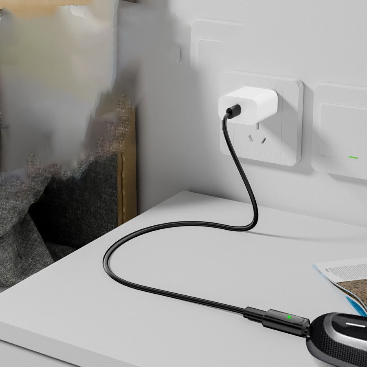 Ein weißer Ladeadapter, der an eine Steckdose angeschlossen ist, mit einem schwarzen Kabel verbunden. Das Kabel führt zu einem schwarzen Gerät.