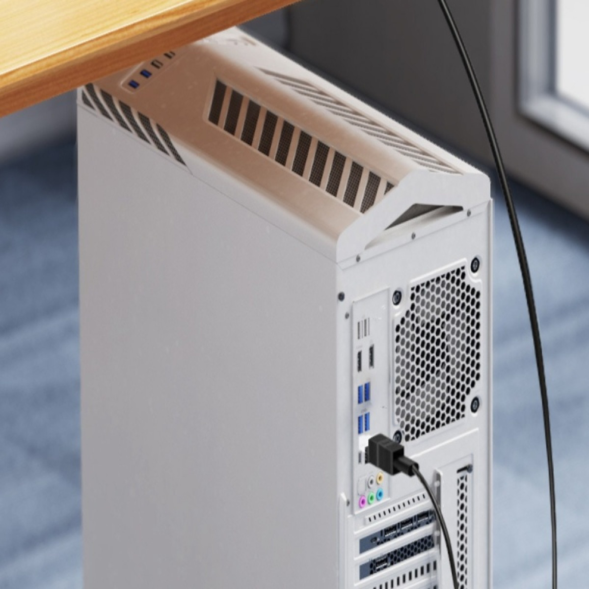 Ein weißer Computerturm unter einem Holzschreibtisch. Er hat ein schwarzes Kabel hinten angeschlossen. Der Hintergrund ist eine verschwommene Büroumgebung.