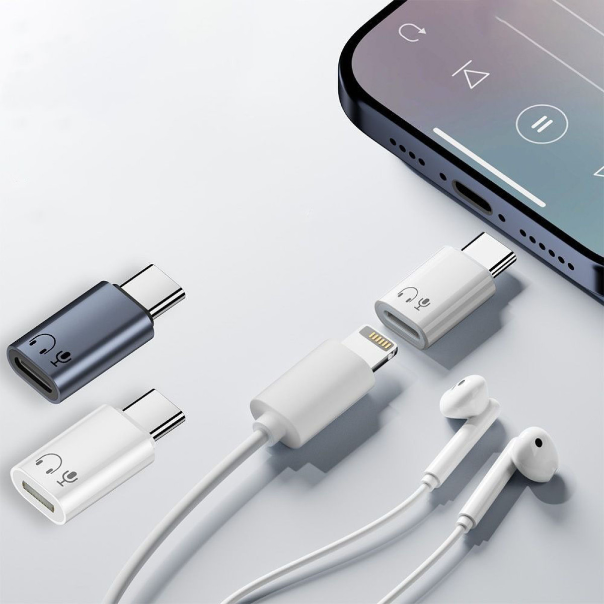 Obraz przedstawia adaptery audio, słuchawki i smartfon. Adaptery są srebrne, białe i szare. Słuchawki są białe. Telefon wyświetla aplikację muzyczną.