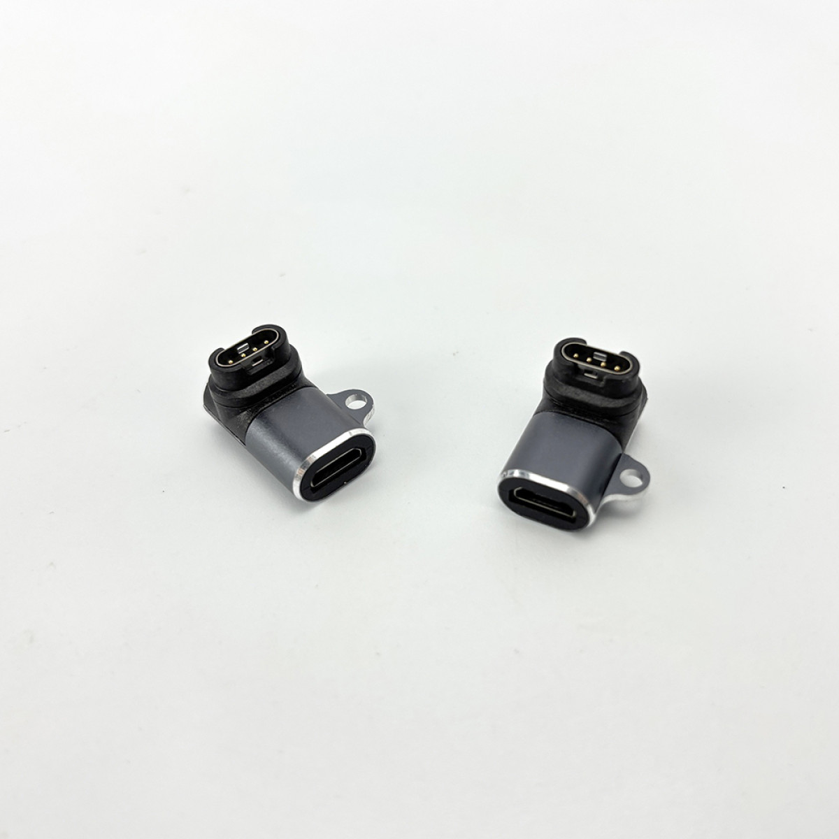 Zwei graue USB-C-Adapter auf weißem Hintergrund. Jeder hat einen schwarzen Stecker und einen silbernen Anschluss, abgewinkelt.