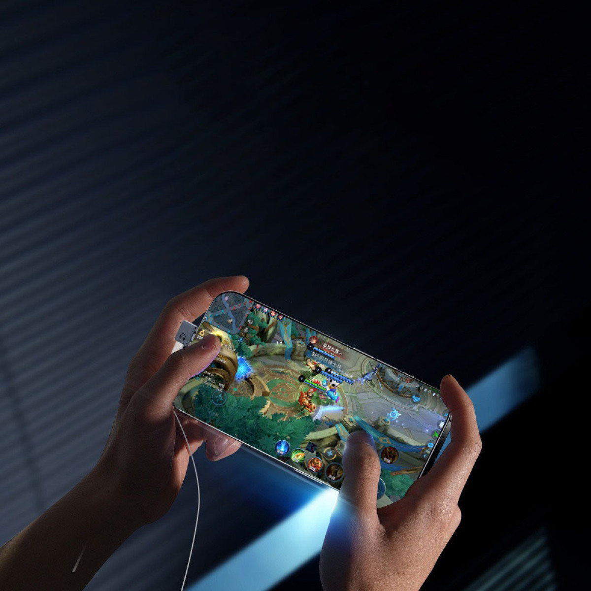 Hände halten ein Telefon und spielen ein Spiel. Der Bildschirm zeigt eine farbenfrohe Kampfszene. Ein weißes Kabel ist am Telefon angeschlossen.