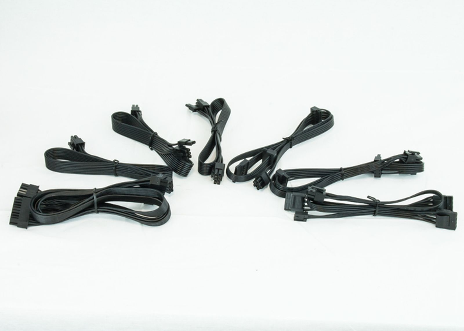 Kilka czarnych kabli zasilających do komputera ułożonych na białym tle.