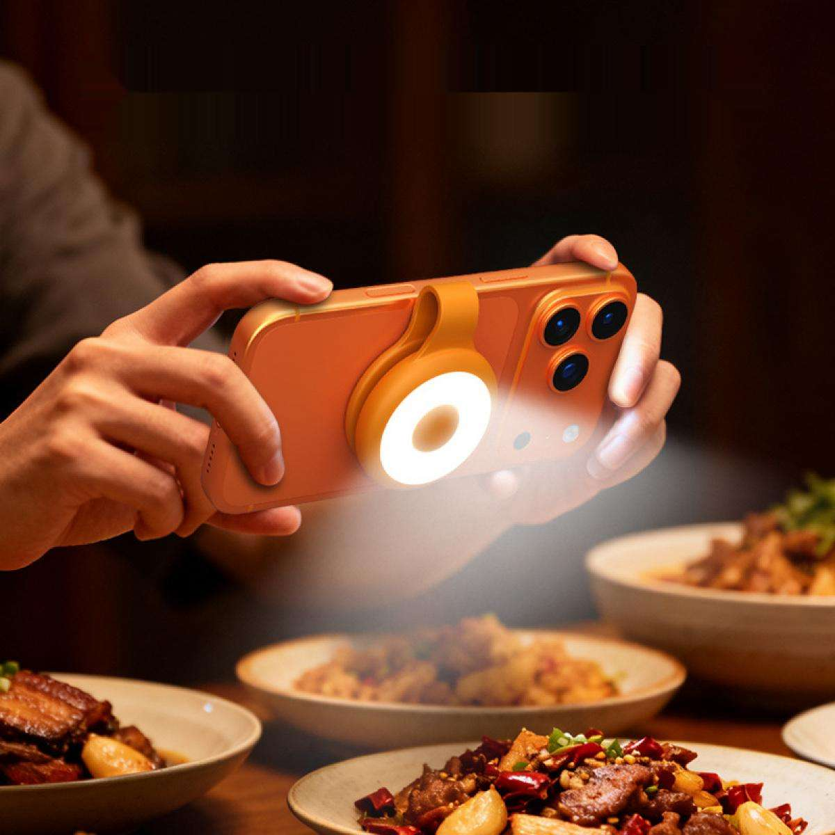 Eine Person hält ein orangefarbenes Telefon mit einem Ringlicht und beleuchtet damit Essen auf Tellern. Der Hintergrund ist verschwommen.