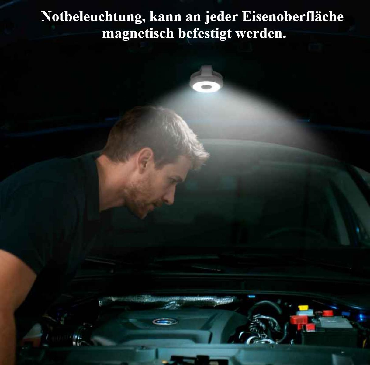 Ein Mann untersucht einen Automotor unter dem Licht einer magnetischen Arbeitsleuchte. Die Szene wird von der Lampe beleuchtet.