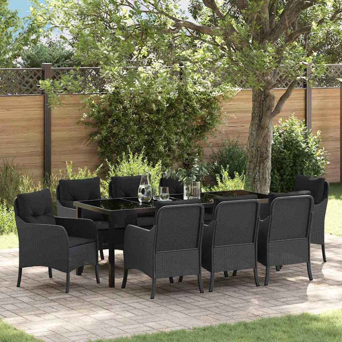 Essgruppe im Freien. Schwarzer Tisch und Stühle auf einer Terrasse. Grünes Gras und Bäume im Hintergrund. Holzzaun.
