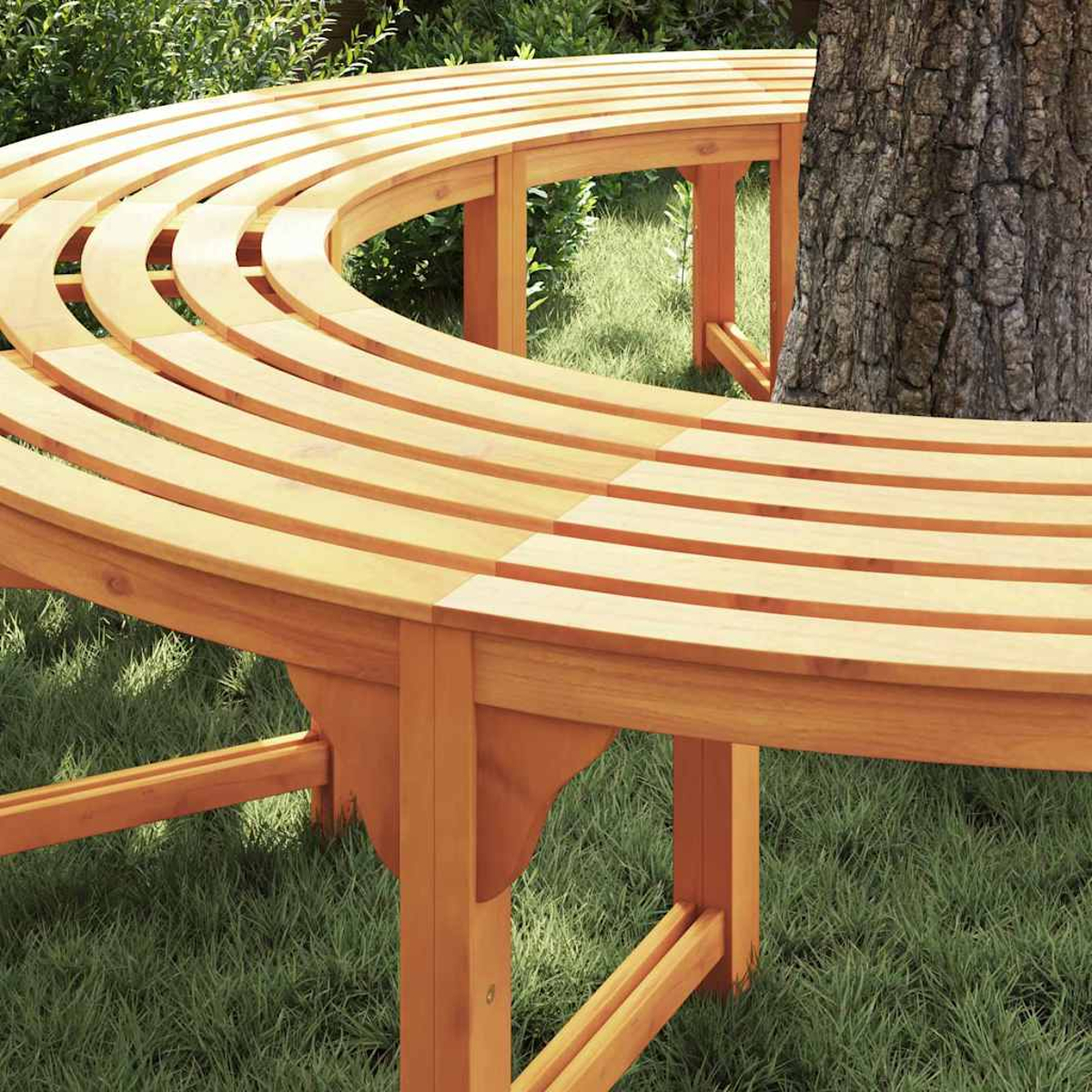 Un banco de madera curvado rodea un árbol. El banco es marrón claro y el árbol tiene corteza áspera. Se ve hierba verde.