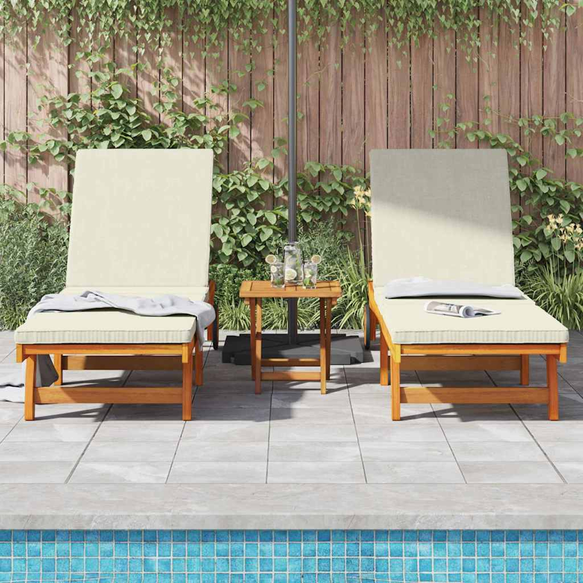 Dos tumbonas beige junto a una piscina con una mesita entre ellas, junto a una valla de madera con plantas verdes.