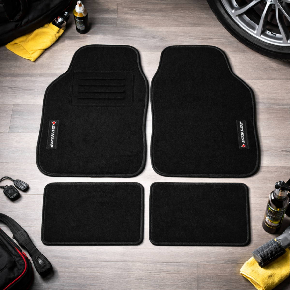 Zwarte Dunlop automatten set op houten vloer. Inclusief voor- en achtermatten, autosleutels, schoonmaakbenodigdheden en een wiel.