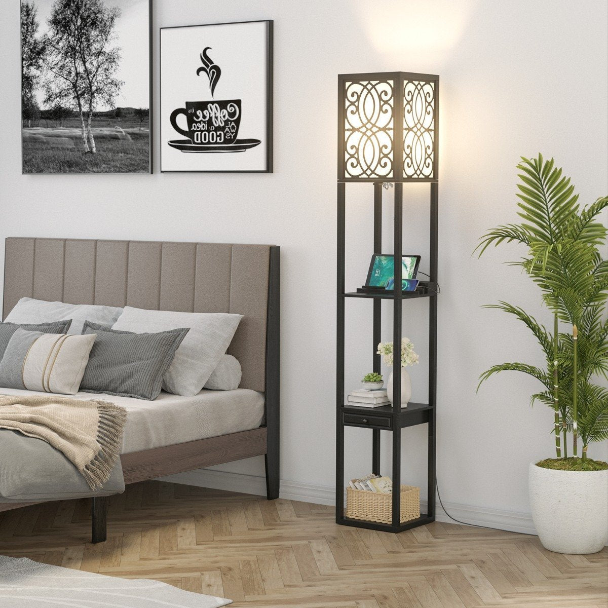 Escena de dormitorio: Cama, lámpara con estantes, planta y obras de arte. La lámpara tiene una pantalla iluminada. Arte mural: taza de café y escena de árbol.
