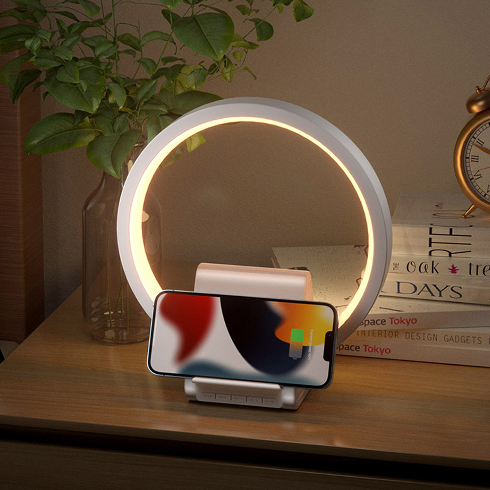 Ein Telefon, das auf einem weißen Ständer geladen wird, mit einem leuchtenden Ringlicht, einem Wecker und einer Pflanze.