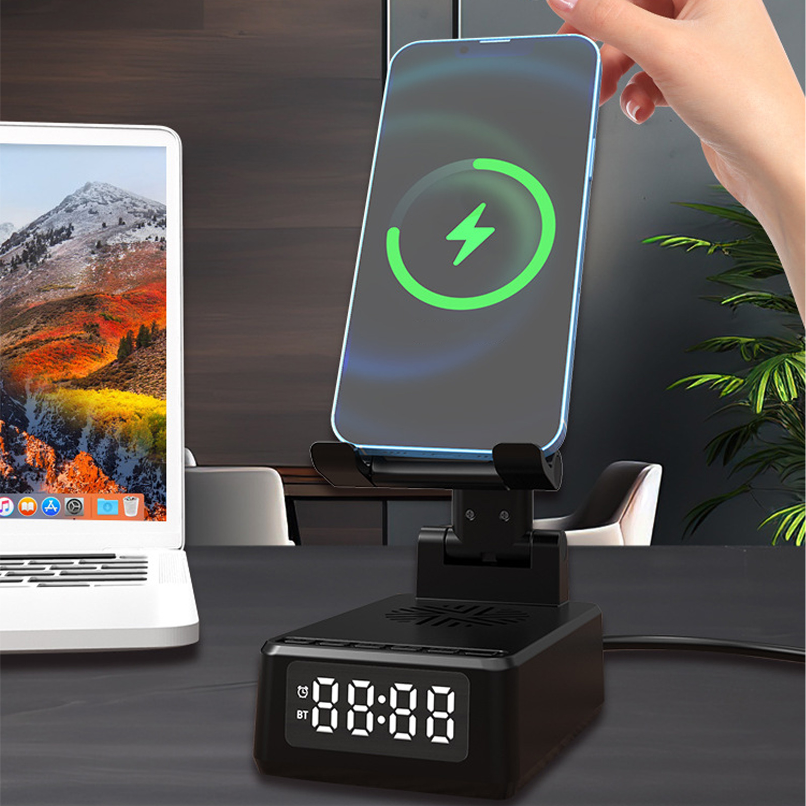 Ein Telefon wird auf einem schwarzen Ständer mit Digitaluhr aufgeladen. Ein Laptop ist im Hintergrund.