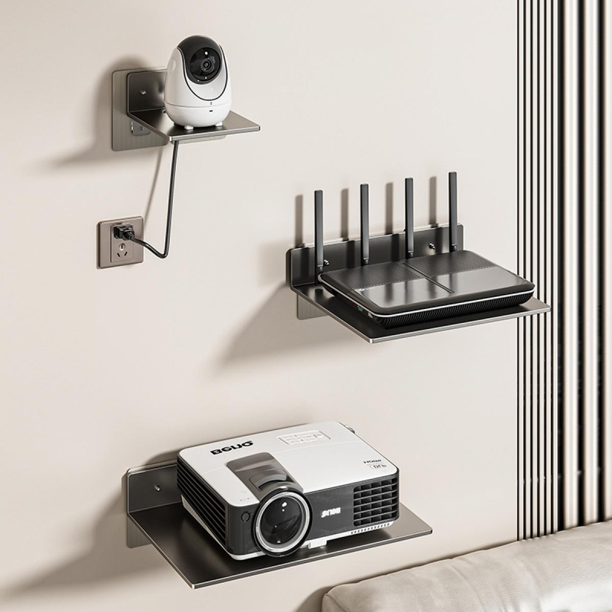 Eine Wand mit drei Regalen. Das obere Regal hält eine Überwachungskamera. Mitte, ein Router. Unten, ein Projektor. Alle sind schwarz und weiß.