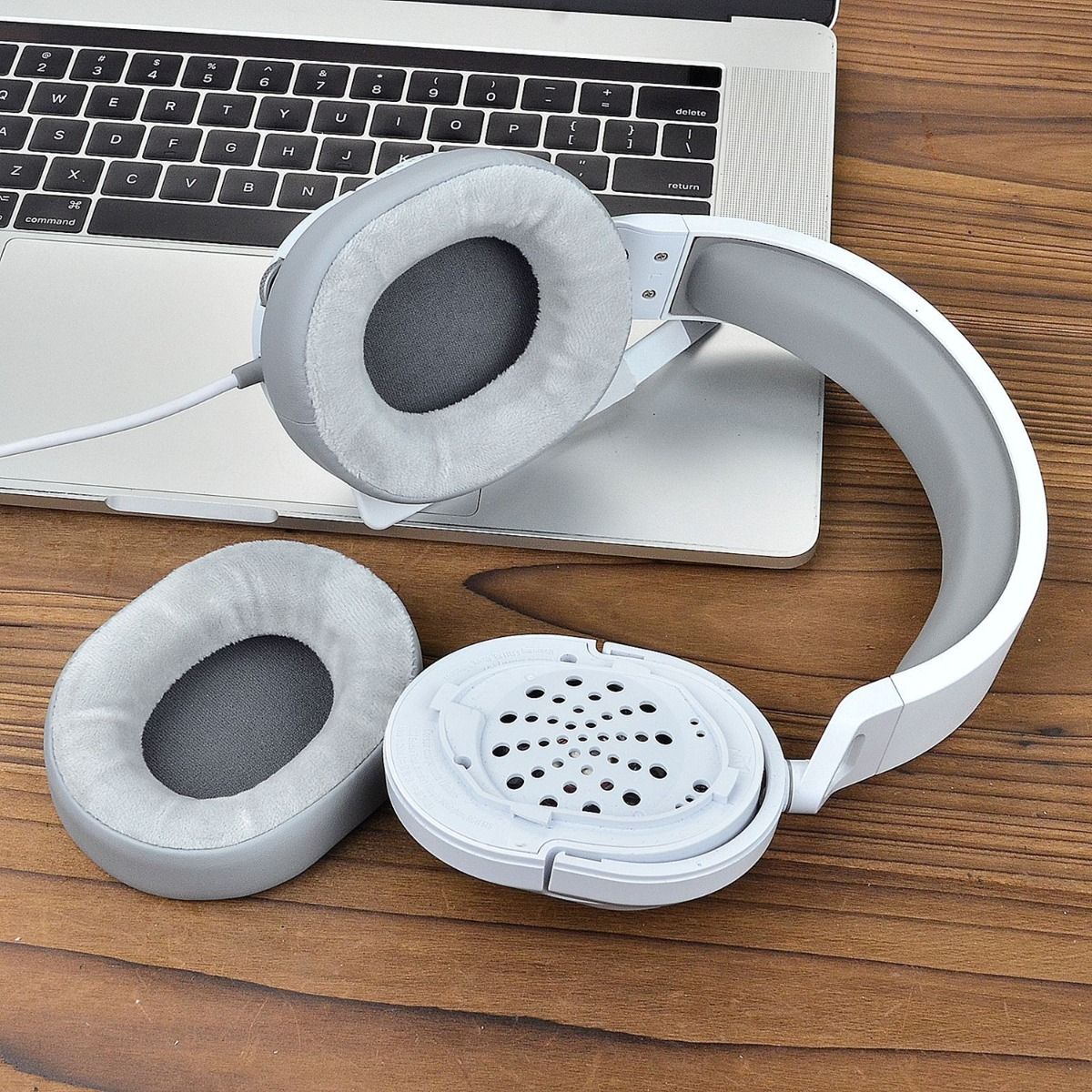 Auriculares blancos y grises desmontados sobre una superficie de madera junto a un portátil.