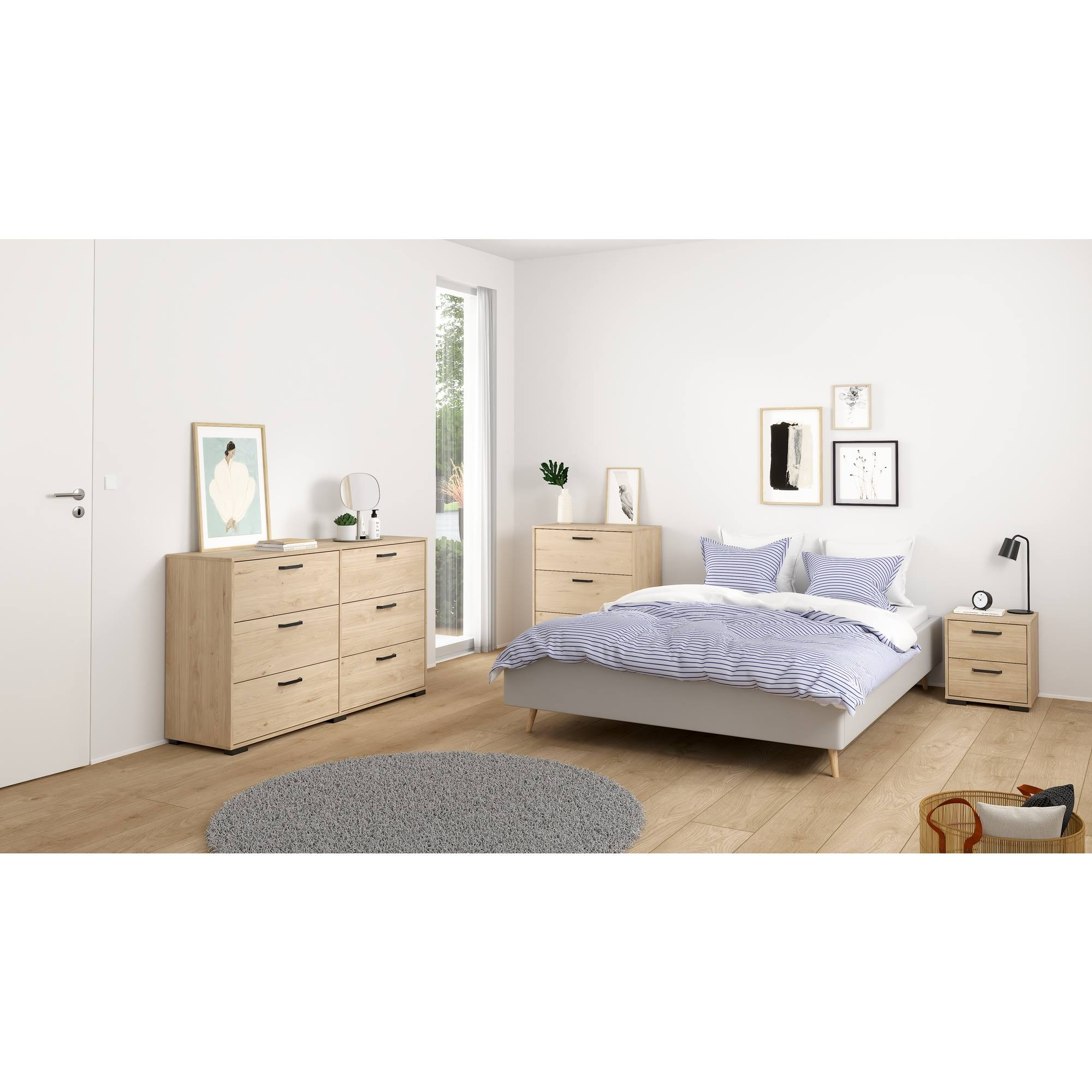 Dormitorio con cama, cómodas y obras de arte. La ropa de cama tiene rayas azules. Alfombra redonda en el suelo de madera.