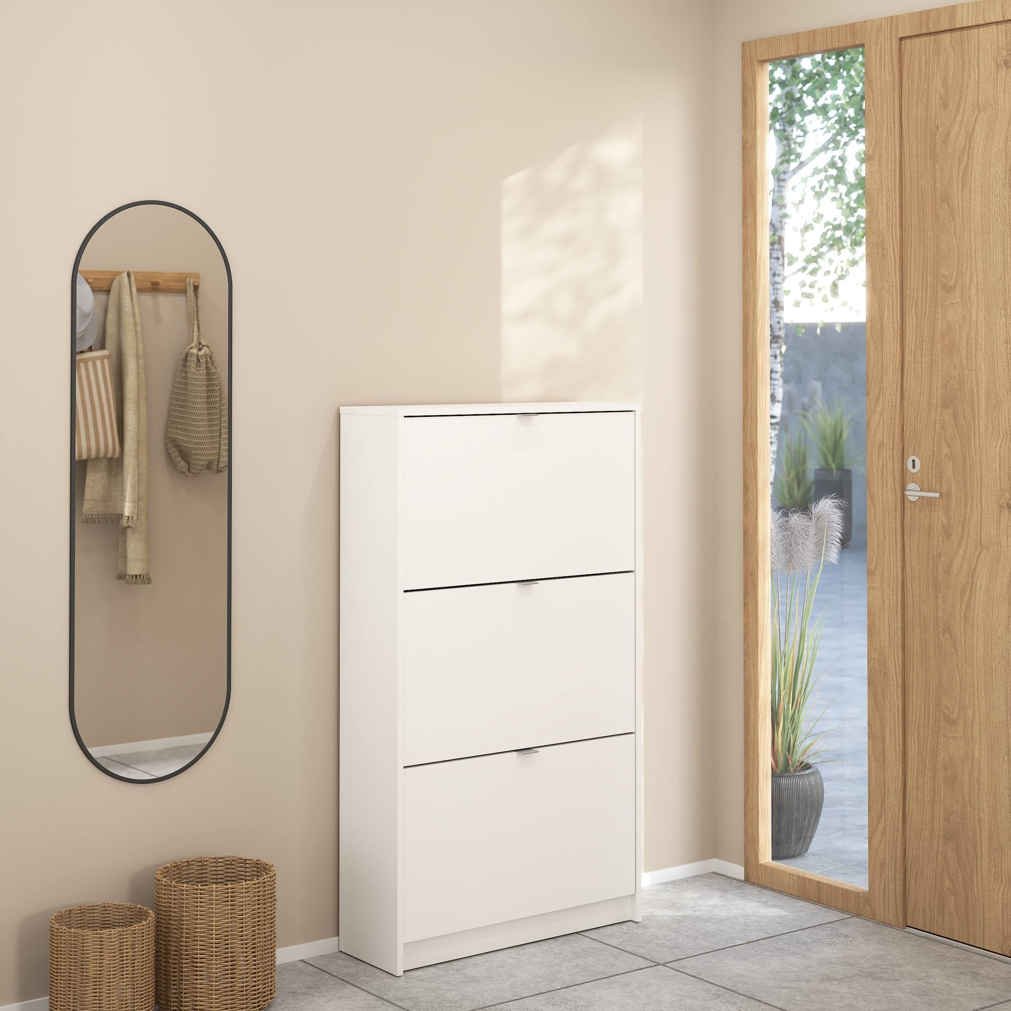 Entrada con zapatero blanco, espejo, puerta y cestos. La puerta conduce a un jardín con plantas.