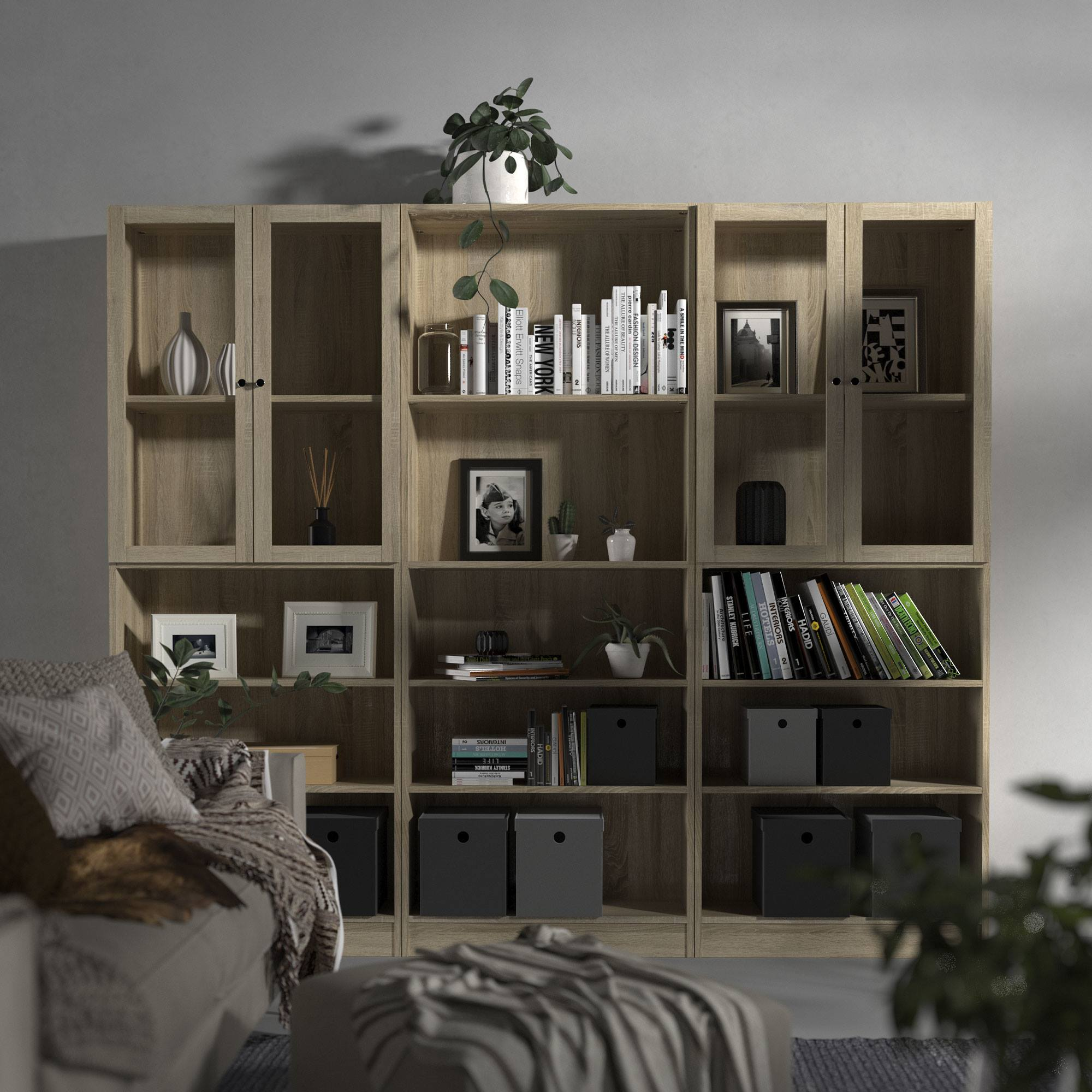 Una estantería de madera llena de libros, decoración y plantas. Un sofá con una manta está en primer plano.