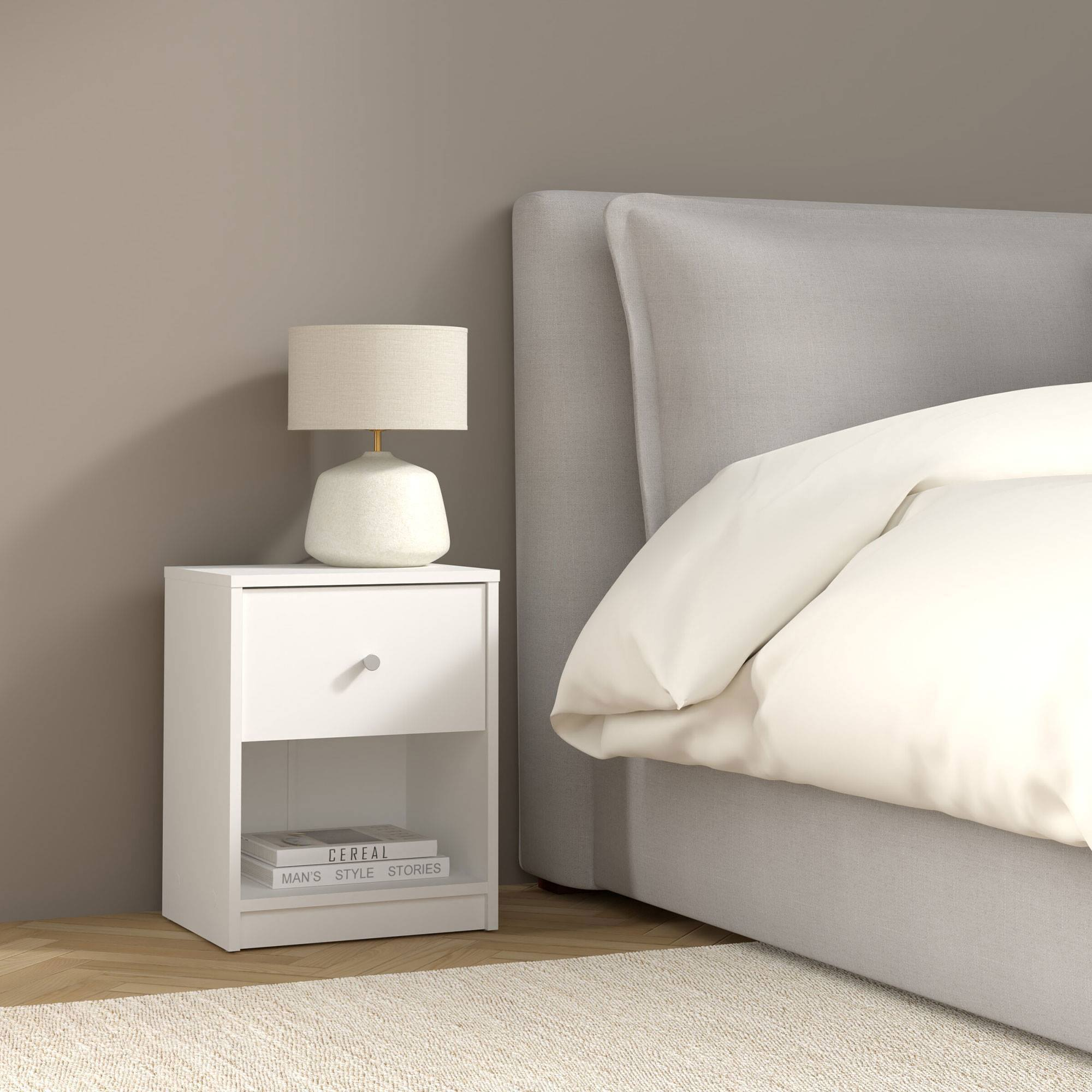 Una mesita de noche blanca con lámpara, libros y cama con ropa de cama blanca.